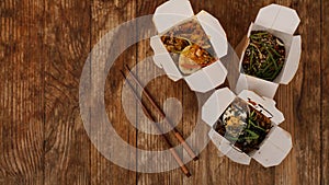 Noodles with pork and vegetables in take-out box on wooden table