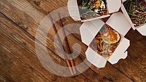 Noodles with pork and vegetables in take-out box on wooden table