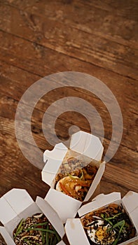 Noodles with pork and vegetables in take-out box on wooden table