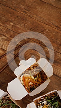 Noodles with pork and vegetables in take-out box on wooden table