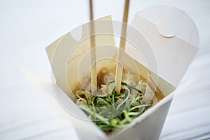 Noodles with pork and vegetables in take-out box on wooden table