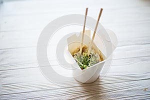 Noodles with pork and vegetables in take-out box on wooden table