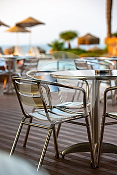 Nook of street cafee with several metal chairs and tables near sea.