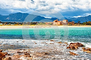 The Nora bay and beach, the medieval Sant\'Efisio church near the shore and mountains in the background