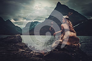 Nordic goddess in ritual garment with hawk near wild mountain lake in Innerdalen valley.