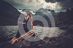 Nordic goddess in ritual garment with hawk near wild mountain lake in Innerdalen valley.