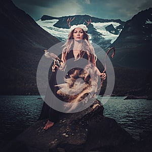 Nordic goddess in ritual garment with hawk near wild mountain lake in Innerdalen valley.