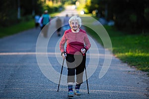 Nordic walking. An elderly woman with ski poles is on the road. Nature.
