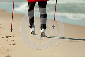 Nordic walking. Female legs hiking on the beach.