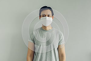 Normal face of man wearing white hygienic mask in grey t-thirt with copy space.