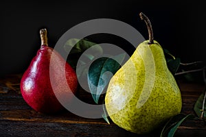 Normal view of a green or packham pear and a red or red battler pear on a table. Dark background. Organic and natural products,