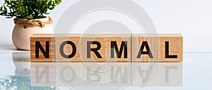 Normal is a word written in black letters on wooden cubes located on a white mirror surface. The world is changing to balance it
