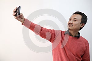 A north east indian manipuri guy taking selfie photograph in a mobile phone isolated in white background with space for photo