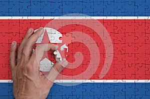 North Korea flag is depicted on a puzzle, which the man`s hand completes to fold