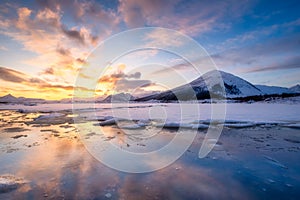 North, Norway. Winter landscape during sunset. Bright sky. Ice and snow on the shore. Reflections on the ice surface. Snowy winter