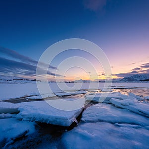 North, Norway. Winter landscape during sunset. Bright sky. Ice and snow on the shore. Reflections on the ice surface. Snowy winter