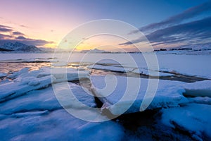 North, Norway. Winter landscape during sunset. Bright sky. Ice and snow on the shore. Reflections on the ice surface. Snowy winter