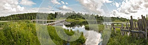 North Russian village Isady. Summer day, Emca river, old cottages on the shore, old wooden bridge and clouds reflections.