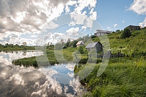 North Russian village Isady. Summer day, Emca river, old cottages on the shore, old wooden bridge and clouds reflections. photo