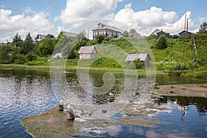 North Russian village Isady. Summer day, Emca river, old cottages on the shore, old wooden bridge and clouds reflections. photo