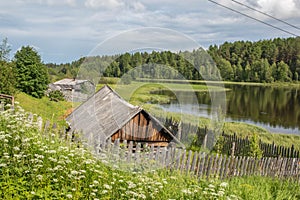 North Russian village Isady. Summer day, Emca river, old cottages on the shore, old wooden bridge and clouds reflections. photo