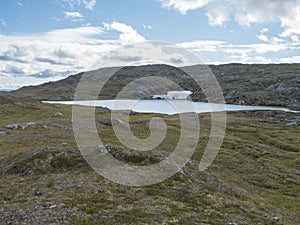 Northern landscape, tundra in Swedish Lapland with blue artic lake with reamains of melting snow cave, green hills and