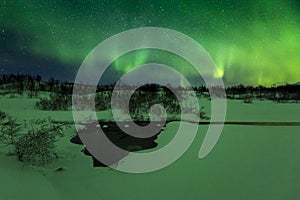 Northern lights above a water stream in a winter landscape.