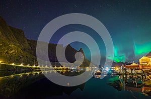 Northern lights Aurora Borealis over illuminated fishing village of reine lofoten islands.