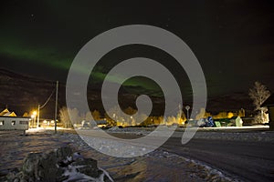 The northern lights aurora borealis rising behind a mountain in a small village in the north of Norway. In the middle of winter