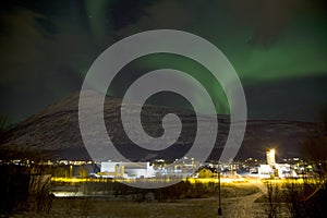 The northern lights aurora borealis rising behind a mountain in a small village in the north of Norway. In the middle of winter