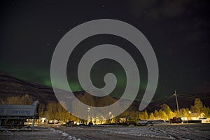 The northern lights aurora borealis rising behind a mountain in a small village in the north of Norway. In the middle of winter