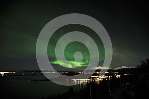 Northern Lights aurora borealis and stars over trees and mountains.