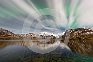 Northern lights behind thin clouds over a mountain range