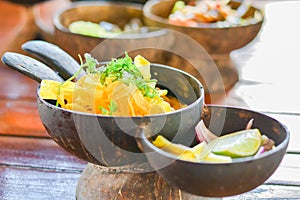 Northern Thai curry noodles with chicken serve in coconut shell on wooden table. Delicious Thai food