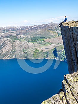 Norway - Boy sitting on a steep cliff with the view on Lysefjorden