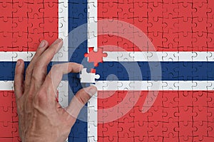 Norway flag is depicted on a puzzle, which the man`s hand completes to fold