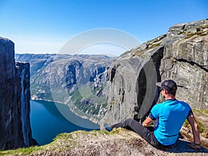 Norway - A man sitting at the edge of a steep mountain with a fjord view