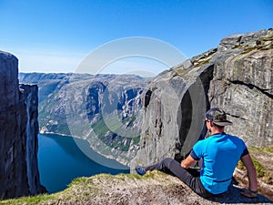 Norway - A man sitting at the egde of a steep mountain with a fjord view