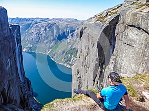 Norway - A man sitting at the egde of a steep mountain with a fjord view