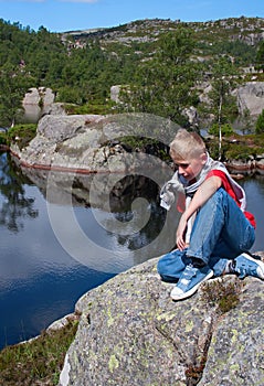Norway. The thoughtful boy sits on a big stone at water