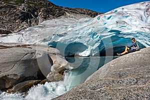 Norway Travel, Young Woman with a backpack admires Nigardsbreen Nigar Glacier arm of Jostedalsbreen located in Gaupne Jostedalen