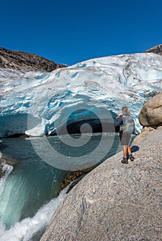 Norway Travel, Young Woman with a backpack admires Nigardsbreen Nigar Glacier arm of Jostedalsbreen located in Gaupne Jostedalen