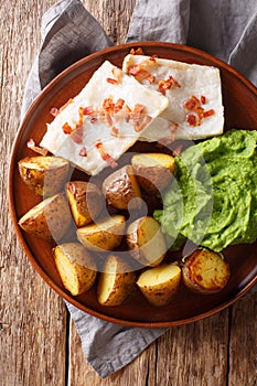 Norwegian cod lutefisk served with pea puree, potatoes and bacon close-up. vertical top view