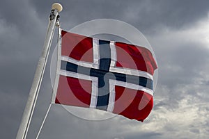 Norwegian flag blowing in strong wind against moody sky