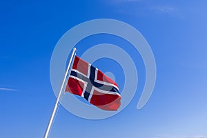 The Norwegian flag, proudly unfurling in the wind atop a flagpole, stands out against a backdrop of a pristine blue sky