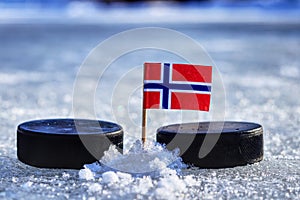 A Norwegian flag on toothpick between two hockey pucks on ice in outdoor. A Norway will playing on World cup in group B. 2019 IIHF