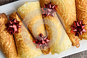 Norwegian Krumkake cookies on a white ceramic plater, rustic dark wood background, red ribbon bows