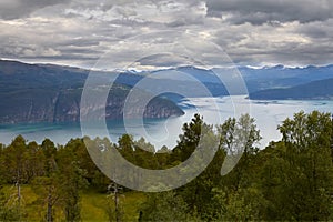 Norwegian landscape. A winding fjord with emerald water. A chain of mountain ranges. Gloomy sky.