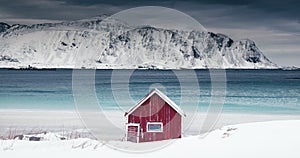 Norwegian red house on the beach coast and mountain hills at snowstorm, Lofoten islands, Norway