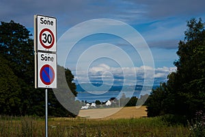 Norwegian roadsigns with houses on the shoreline under a blue cloudy sky in Trondheim, Norway.